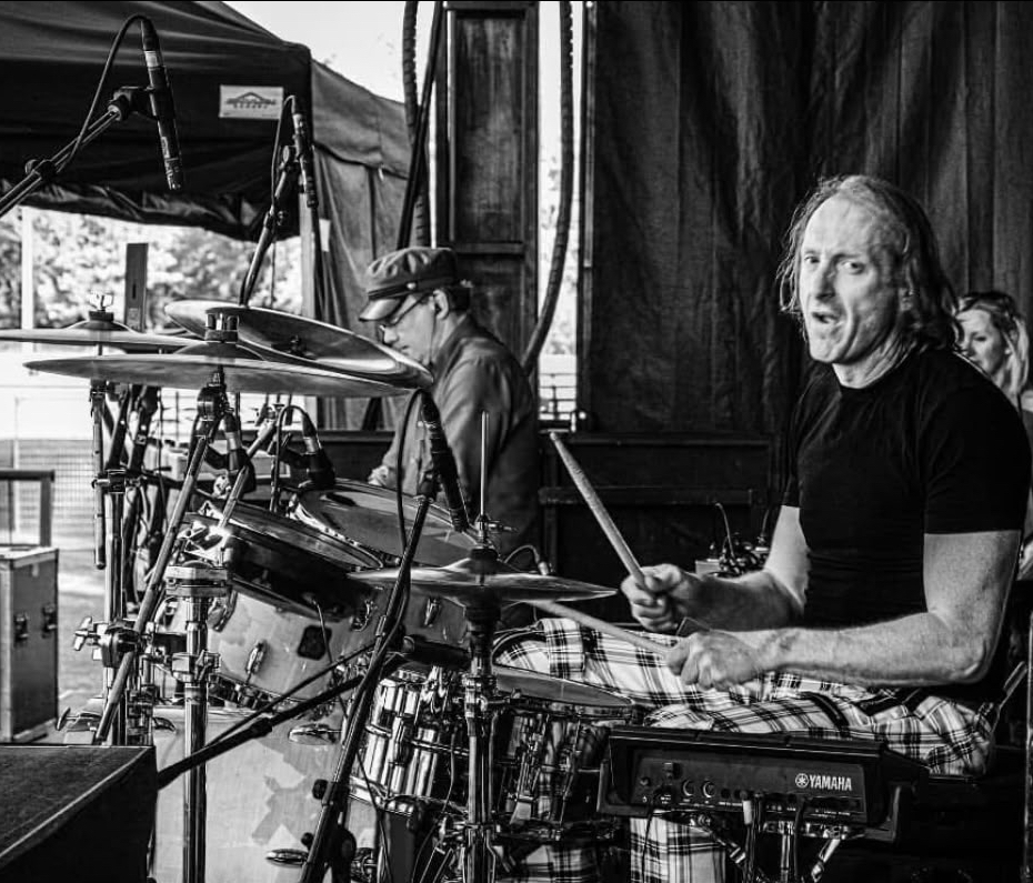 Antony mid-fill behind his drum kit on an outdoor stage, in black and white