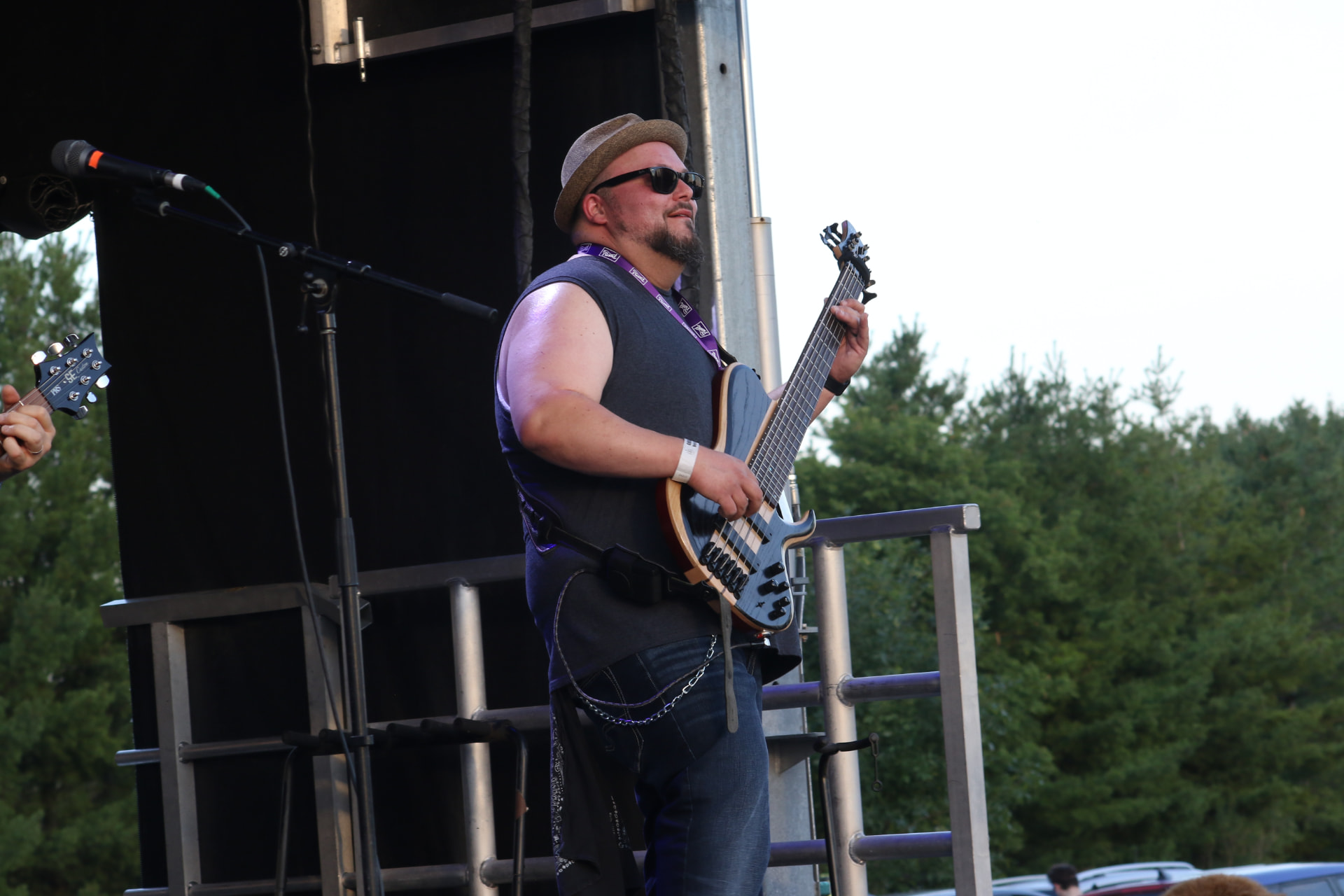 Matt in a fedora and sunglasses playing a six-string bass on an outdoor festival stage