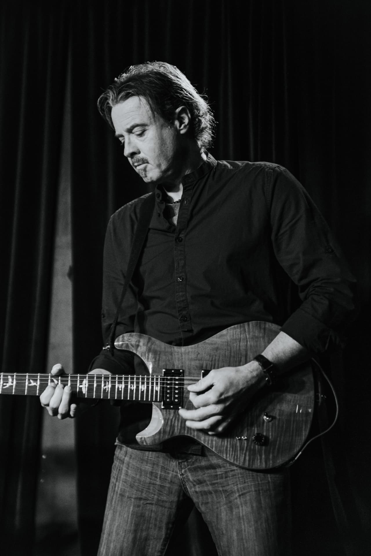 Dave playing a PRS guitar in front of a dark curtain