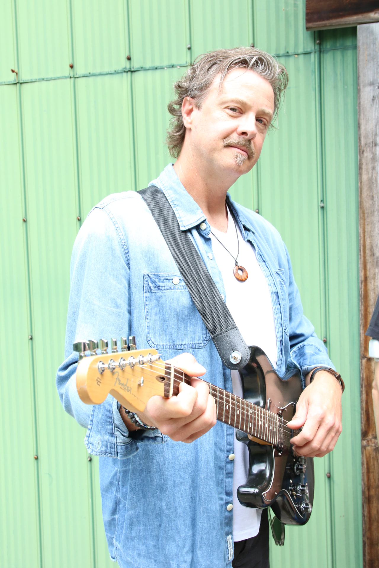 Dave with a black Fender in front of a green corrugated wall