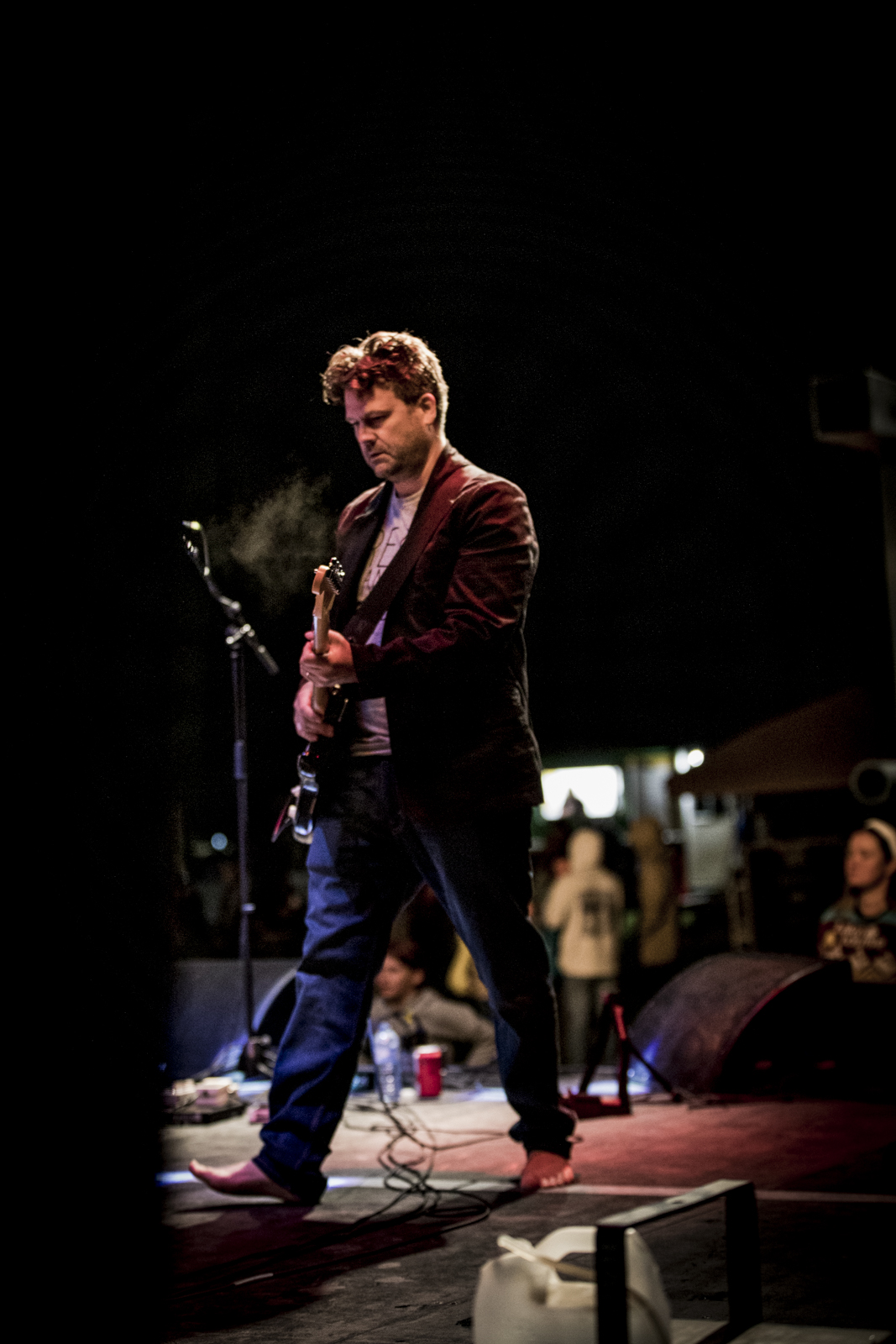 Guitarist alone at the front of a dark stage between songs