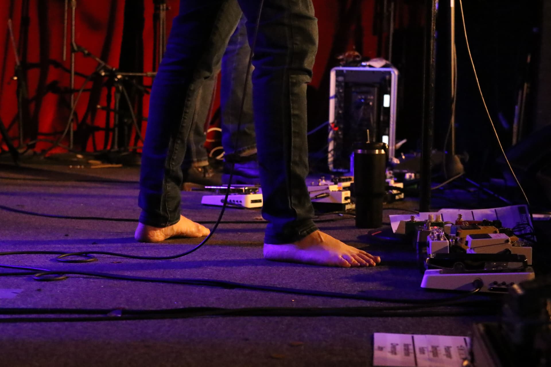 Bare feet on stage next to a pedalboard under purple light